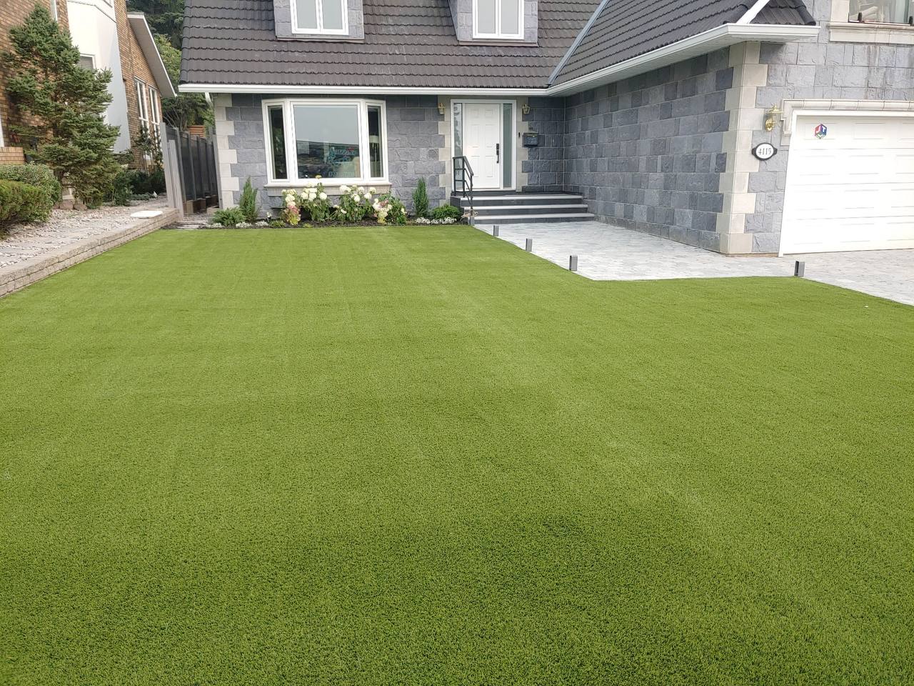 Finished artificial turf front yard installation with stone facade home and paver walkway